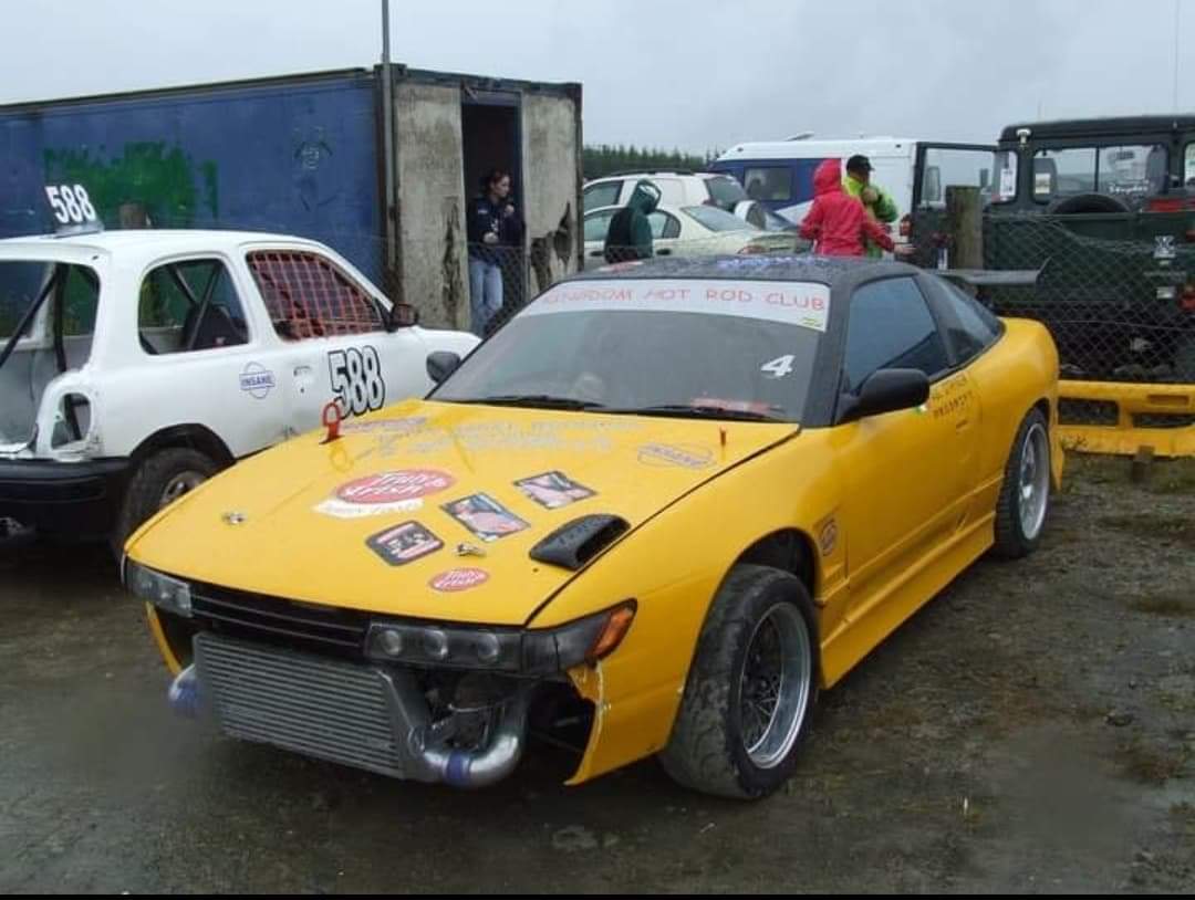 A yellow track car photographed in a paddock